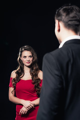 selective focus of beautiful woman in red dress with man on foreground isolated on black