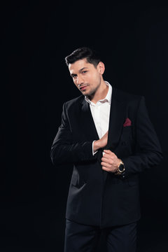 handsome man posing in in suit and looking at camera isolated on black
