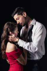 handsome man embracing beautiful woman in red dress isolated on black