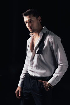 handsome man in white shirt and hand in pocket looking at camera while posing isolated on black