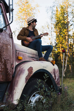 Young man sitting on a broken truck, playing the ukulele
