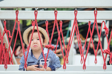 Closeup cute asian kid with bored face on a bridge in playground background