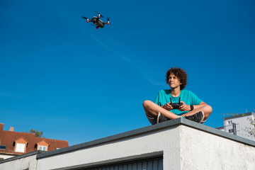 Boy navigating a flying drone, sitting on garage roof