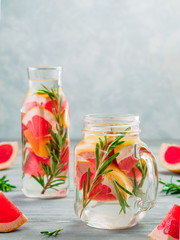 infused detox water with grapefruit and rosemary in mason jar and glass bottle on gray wooden...