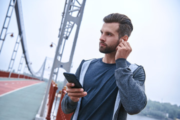Serious young sportsman listening music and using fitness tracker and smartphone outdoors