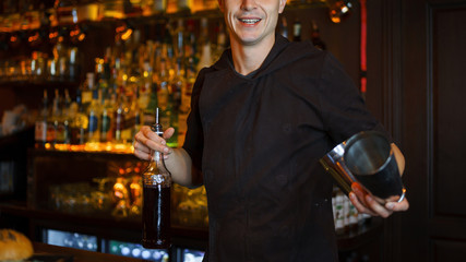 Handsome young barman man with a smile makes a cocktail at the bar