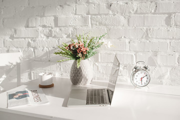 laptop near business newspaper, cup and vase with flowers in kitchen