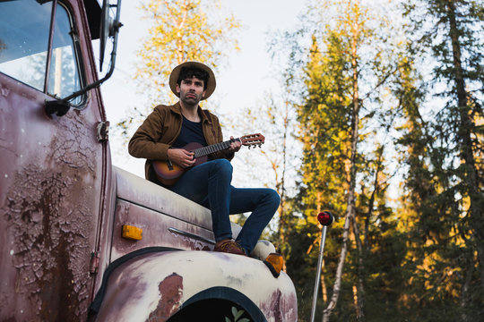 Young man sitting on a broken truck, playing the ukulele