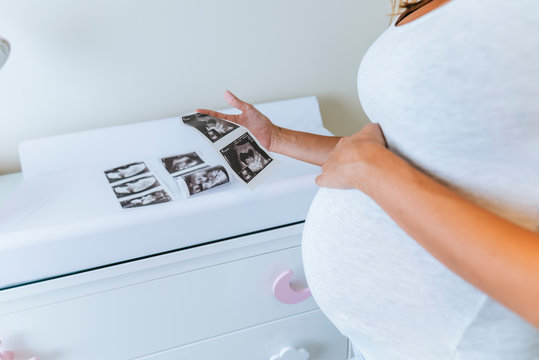 Close-up of pregnant woman looking at ultrasound images in baby room