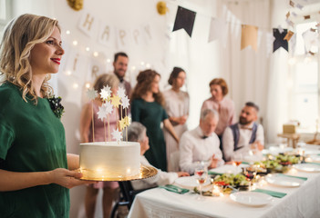 A young woman holding a birthday cake on an indoor party.