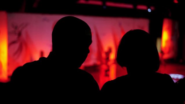 Video From The Back Silhouette Man And Woman Sitting Looking Performance Or Presentation In The Theater Background Red Pink Light Audience Concert Hall Stage Play Abstract Audience Slow Motion