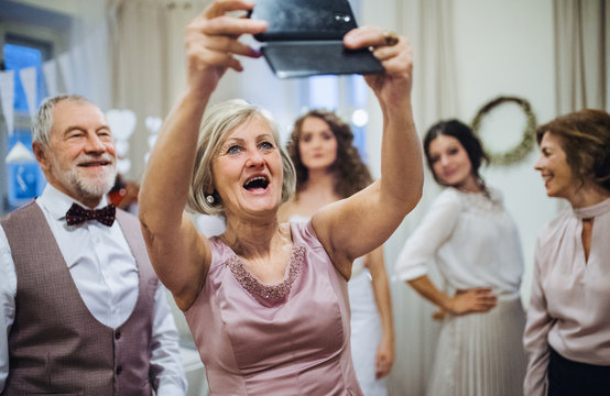 A senior woman with husband on wedding or birthday party, taking selfie with smartphone. - Powered by Adobe