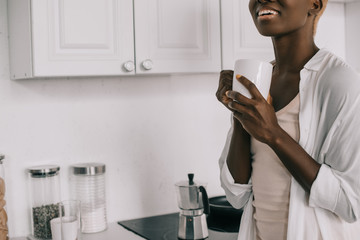cropped view of cheerful african american woman with cup of coffee