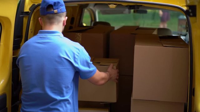 Courier in blue uniform loads boxes into car.