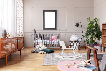 White wooden rocking horse on patterned carpet in elegant mid century baby room interior, real photo with mockup poster on the empty grey wall