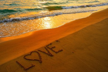 Valentines day concept, love heart shape handwriting on sand beach in sunset and golden ocean.