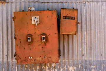 Old rusted iron electricity box with a textured metallic sheet background