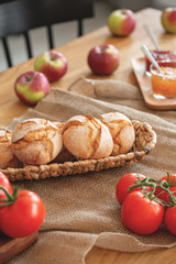 Close-up on tomatoes and loafs on wooden table with apples in dining room interior. Real photo