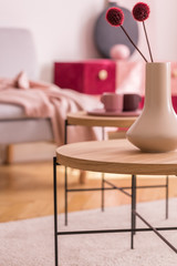 Red flowers in white vase on round wooden table in living room interior with carpet. Real photo