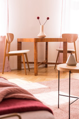 Chairs at wooden table with flowers in bright apartment interior with pink carpet. Real photo