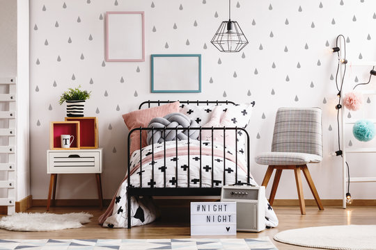 Scandinavian bedroom interior with single metal bed, wooden nightstand and grey chair, real photo