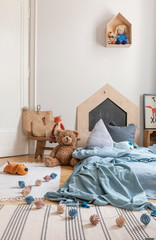 Cotton balls and plush toy next to blue bed in kid's bedroom interior with carpet. Real photo