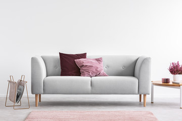 Lilac and burgundy pillows on grey settee in bright living room with heather on coffee table and...