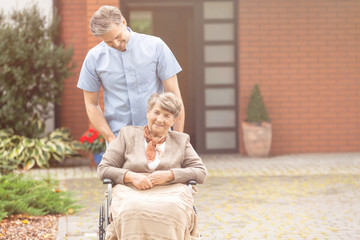 Smiling handsome male nurse and senior pensioner on wheelchair in the garden of nursing home