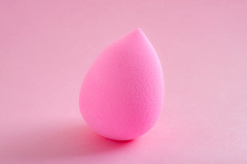 Face foundation application tool and makeup products concept with a beauty blender sponge isolated on a pink background