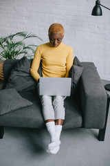 focused african american woman with short hair sitting on sofa and using laptop