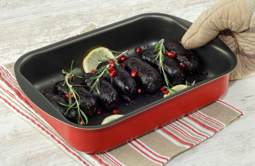 Baked in oven blood pudding sausages in baking dish with seasoning and rosemary and lemon on table...
