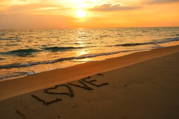 Valentines day concept, love heart shape handwriting on sand beach in sunset and golden ocean.