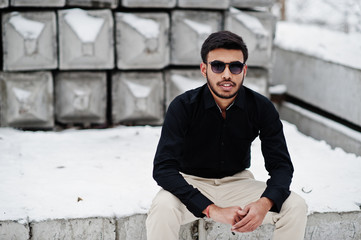 Obraz premium Casual young indian man in black shirt and sunglasses posed against stone blocks.