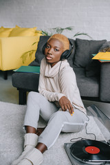 african american woman sitting on carpet and listening music in headphones