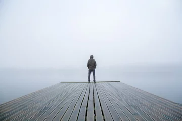  Young man standing alone on edge of footbridge and staring at lake. Mist over water. Foggy air. Early chilly morning in autumn. Beautiful freedom moment and peaceful atmosphere in nature. Back view. © fotoduets
