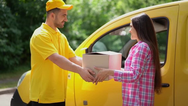 Delivery guy in yellow uniform gives parcel to female customer near car