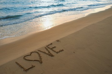 Valentines day concept, love heart shape handwriting on sand beach in sunrise and blue ocean.
