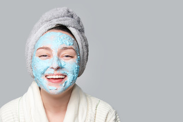 Woman applying facial clay mask at spa salon or at home, skincare theme. Face mask, spa beauty treatment with copy space on gray background.