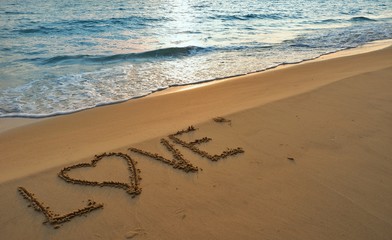 Valentines day concept, love heart shape handwriting on sand beach in sunrise and blue ocean.