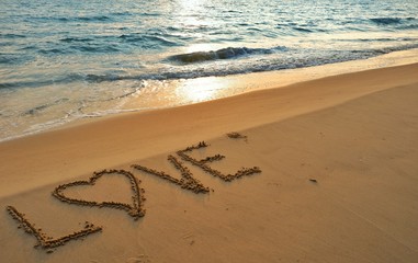 Valentines day concept, love heart shape handwriting on sand beach in sunrise and blue ocean.
