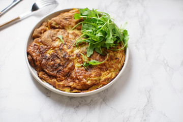 Tortilla omelette with sliced potatoes and herbs on marble table