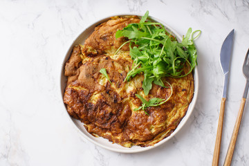 Tortilla omelette with sliced potatoes and herbs on marble table