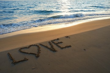 Valentines day concept, love heart shape handwriting on sand beach in sunrise and blue ocean.