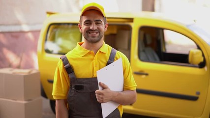 Portrait of smiling courier with clipboard standing near yellow van
