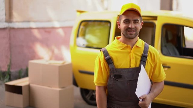 Portrait of smiling courier with clipboard standing near yellow van