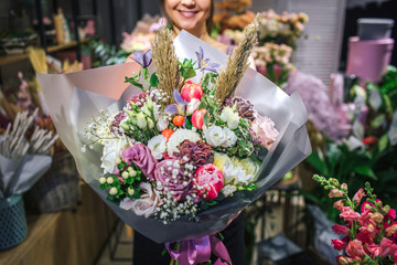 Nice and colorful bouqette of different flowers. Female florist hold it and smile. She is in flower shop. Cut view. Close up. - obrazy, fototapety, plakaty