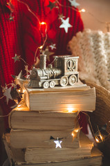 Winter sweater laid on a chair with a books and locomotive, train of Christmas decorations. Coniferous branch and garland, closeup