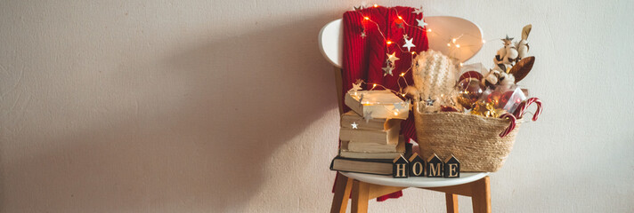 Winter sweater laid on a chair with a basket of Christmas decorations, books. Holiday decoration with the inscription HOME. 