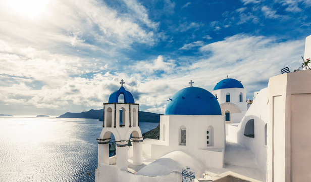 Fototapeta Churches in Oia, Santorini island in Greece, on a sunny day with dramatic sky. Scenic travel background.