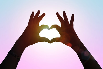 Hands in shape of love heart. Female door hands in the form of heart against the pink blurred pass sun flare. Healthcare and Valentine's day concept.
